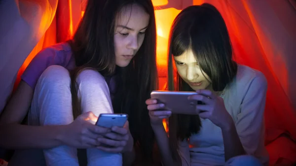 Portrét dvou dospívajících dívek s chytrými telefony pod deku v noci — Stock fotografie