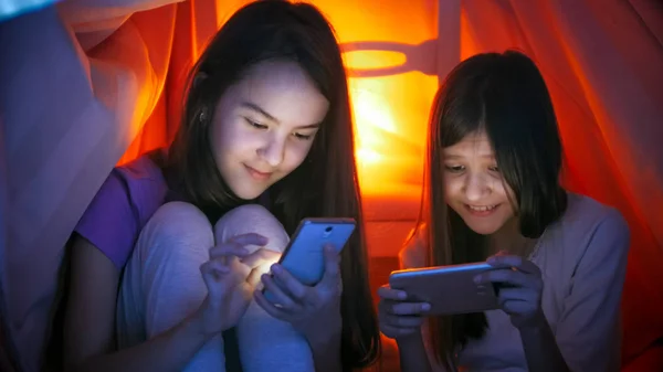 Retrato de duas meninas bonitos em pijama com telefones celulares à noite — Fotografia de Stock