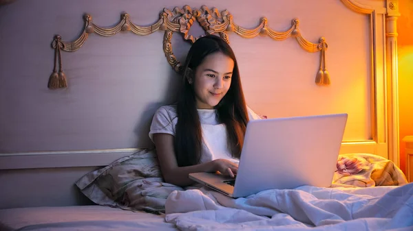 Menina sorridente bonita usando laptop na cama à noite — Fotografia de Stock