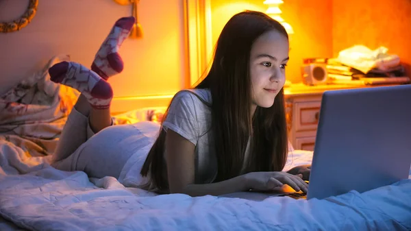 Retrato de hermosa chica sonriente acostada en la cama y el uso de ordenador portátil —  Fotos de Stock
