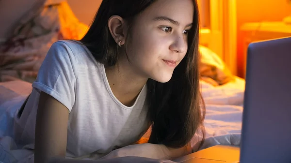 Retrato de menina bonita deitada na cama e navegando na internet no laptop à noite — Fotografia de Stock