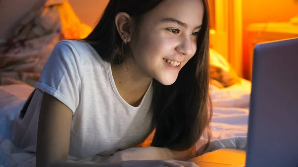 Retrato de menina sorridente feliz deitada na cama e tendo videochamada no laptop à noite — Fotografia de Stock