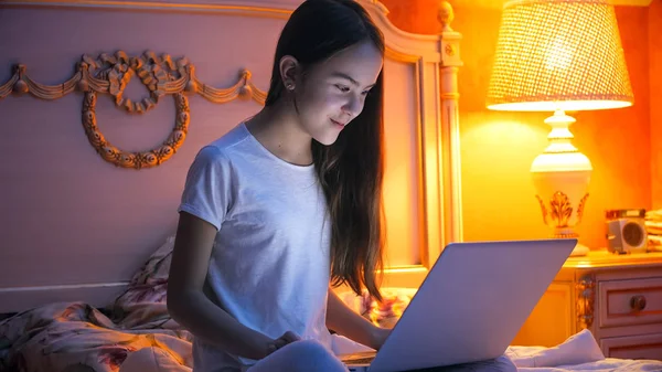 Krásná mladá dívka sedící na posteli v noci s notebookem — Stock fotografie