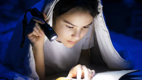 Closeup portrait of teenage girl lying under blanket and reading book — Stock Photo, Image