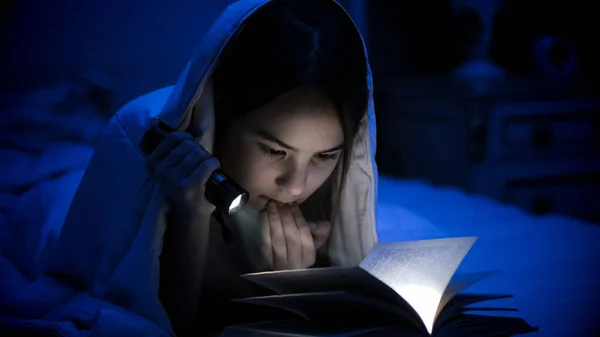 Foto da menina com lanterna leitura livro assustador sob cobertor — Fotografia de Stock