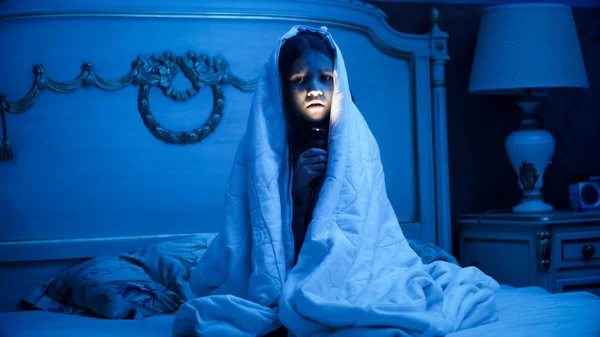 Foto de menina cobrindo sob cobertor segurando lanterna no quarto escuro — Fotografia de Stock