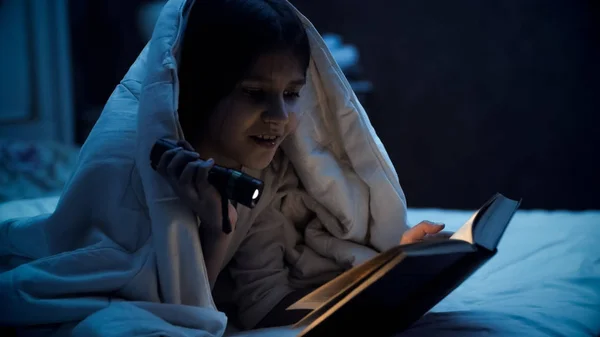 Portret uśmiechnięta dziewczyna czytania książki z latarka w nocy — Zdjęcie stockowe