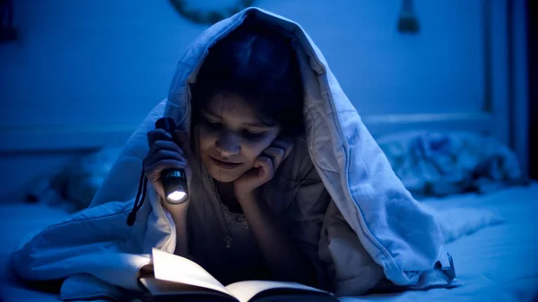 Портрет девочки-подростка, читающей книгу в постели ночью — стоковое фото