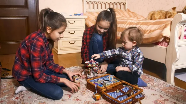 Dos niñas mayores jugando con un niño pequeño en el dormitorio —  Fotos de Stock