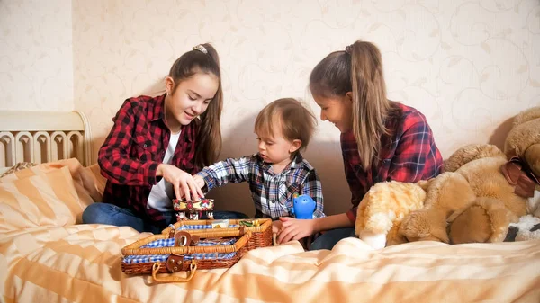 Две девочки-подростки играют со своим младшим братом с игрушками на кровати — стоковое фото