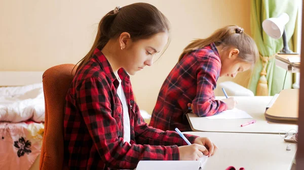 Dos chicas adolescentes haciendo deberes en el dormitorio detrás del escritorio —  Fotos de Stock