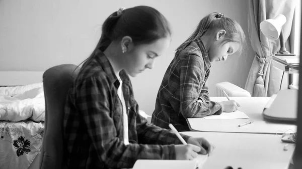 Черно-белый портрет двух девочек-подростков, делающих домашнее задание в спальне — стоковое фото