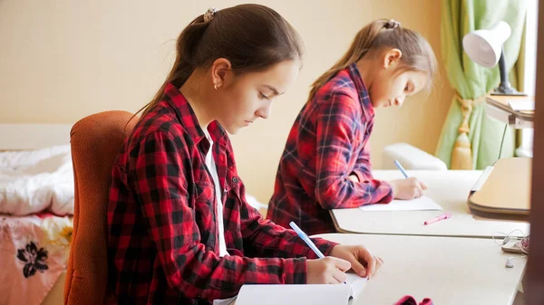 Two teenage girls sitting at big window and doing homework — Stock Photo, Image