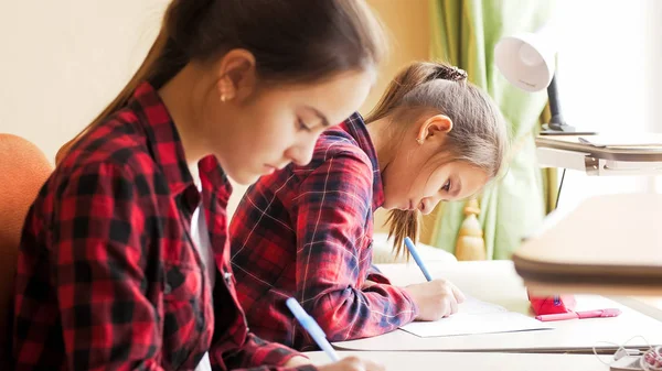 Portrait of two teenage girls sitting behind desk and writing with pens — Stock Photo, Image