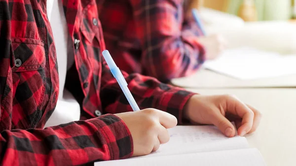 Imagen de primer plano de una adolescente sosteniendo la pluma y escribiendo tareas — Foto de Stock