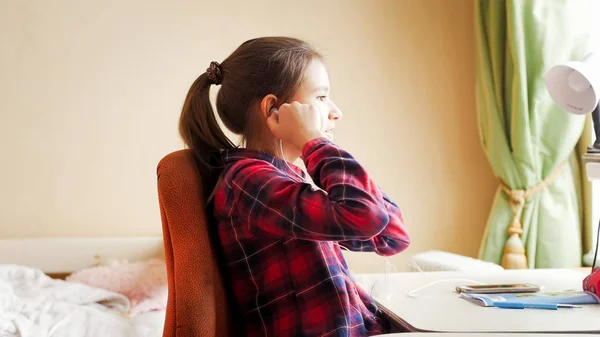 Portrét dospívající dívka uvedení na earphonew zároveň dělat domácí úkoly — Stock fotografie