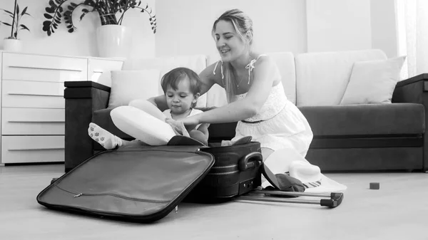 Mignon sourire tout-petit garçon assis dans la valise tandis que la mère emballer des choses pour voyager — Photo