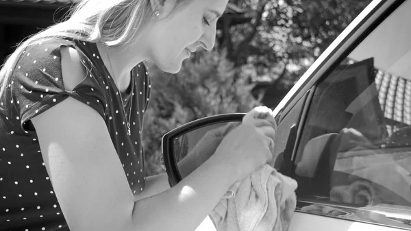 Ritratto in bianco e nero di giovane donna guida pulizia specchi laterali auto — Foto Stock