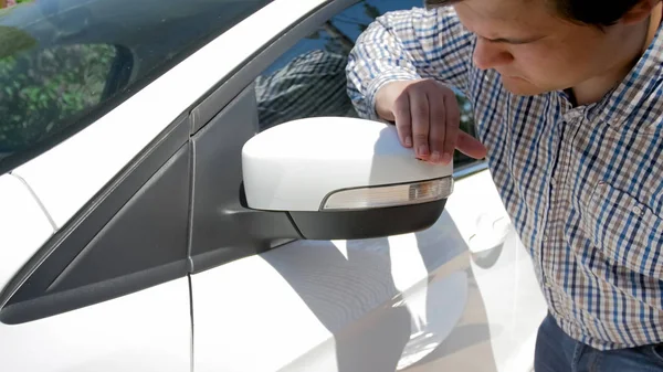 Foto de primer plano del conductor masculino joven mirando el espejo lateral del coche rayado —  Fotos de Stock