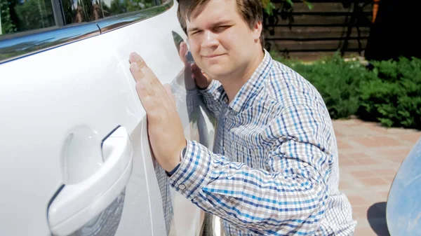 Zbliżenie portret młodzieńca uśmiechający się sprawdzanie lakieru przed kupnem nowego samochodu — Zdjęcie stockowe