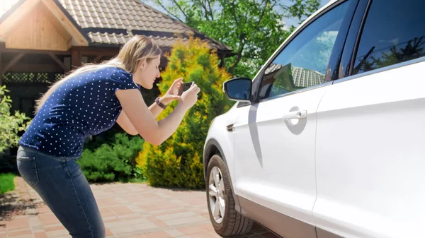 Mujer joven tomando fotografías de su coche en el teléfono móvil — Foto de Stock