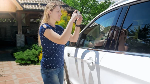 Joven mujer sonriente haciendo fotografías de su coche viejo para venderlo en línea — Foto de Stock