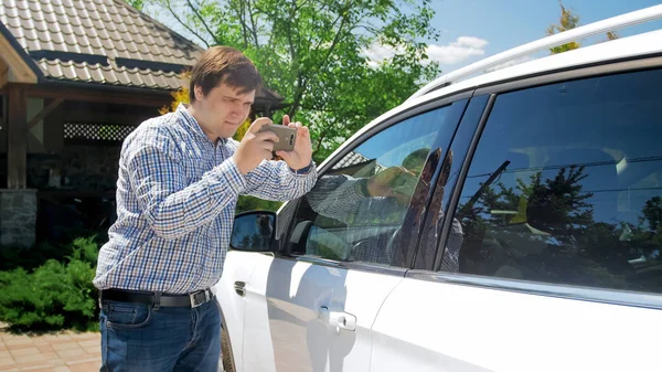 Молодой человек делает фотографии на смартфоне своей машины — стоковое фото