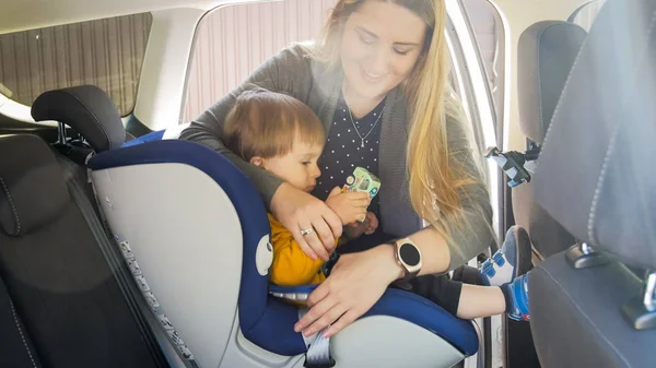 Retrato de la joven madre poniendo a su hijo pequeño en el asiento de seguridad del coche —  Fotos de Stock