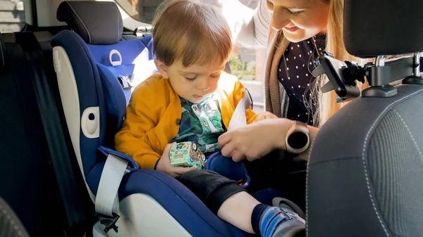 Imagen de primer plano de la madre joven ajustando cinturones en el asiento de seguridad para niños —  Fotos de Stock