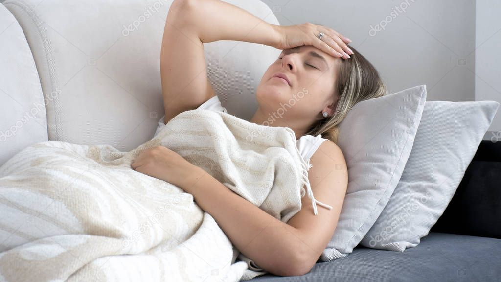 Photo of young woman with migraine lying on sofa at home