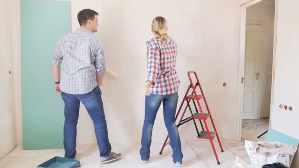 Imágenes en cámara lenta de feliz pareja alegre bailando mientras pintan paredes con rodillo de pintura en su nuevo apartamento bajo renovación — Vídeos de Stock