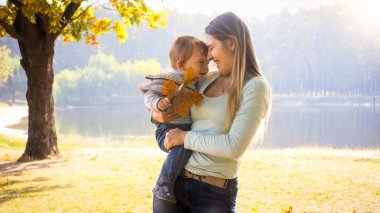 Onun çok güzel yürümeye başlayan çocuk sonbahar Park kucaklayan mutlu gülen anne portresi