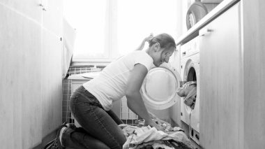 Siyah beyaz resim yükleme genç kadının evde çamaşır makinesine Çamaşırhane giysiler.