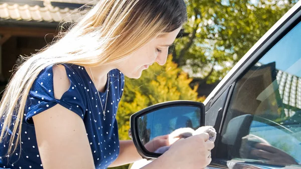 Joven mujer sonriente limpiando sus espejos laterales del coche con tela — Foto de Stock