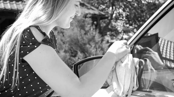 Foto em preto e branco de sorrir jovem mulher polir e limpar janelas do carro — Fotografia de Stock