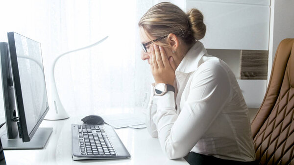 Portrait of bored young woman sitting in office and looking at computer screen
