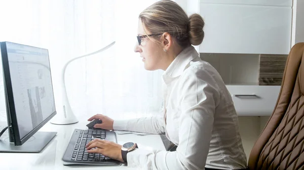 Schöne junge Frau sitzt hinter Schreibtisch und benutzt Computer — Stockfoto