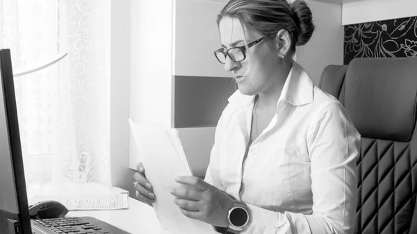 Schwarz-Weiß-Foto der schönen jungen Geschäftsfrau, die im Büro mit Dokumenten arbeitet — Stockfoto