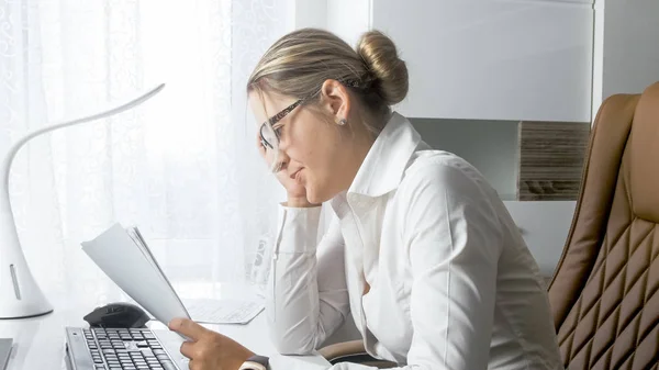 Portret van overstuur en benadrukte zakenvrouw achter bureau zitten en kijken naar documenten — Stockfoto