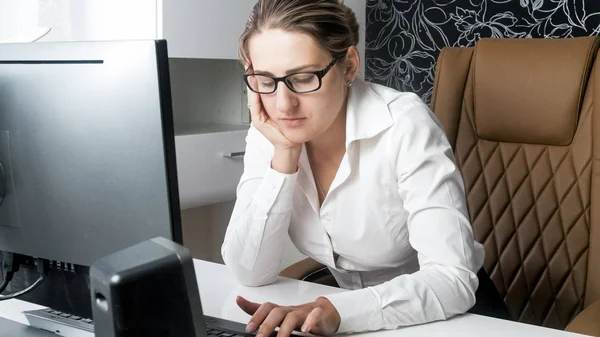 Portrait of overworked young woman leaning on her hand while working on computer — Stock Photo, Image