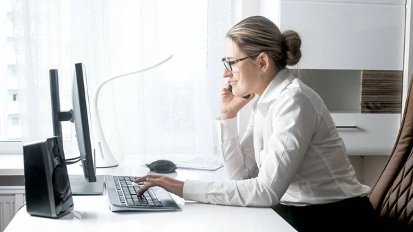 Schöne lächelnde Geschäftsfrau, die im Büro mit dem Handy spricht — Stockfoto