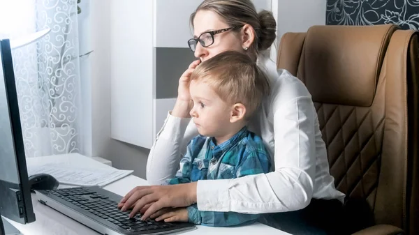 Young businesswoman workinng with her toddler son from home office — Stock Photo, Image