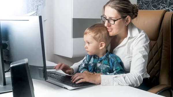 Söta leende pojke med mor affärskvinna arbetande i kontor — Stockfoto