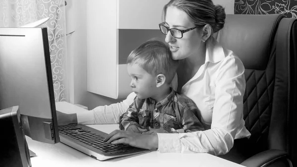 Чорно-білий портрет молодої жінки, яка працює в офісі зі своєю 2-річною дитиною — стокове фото