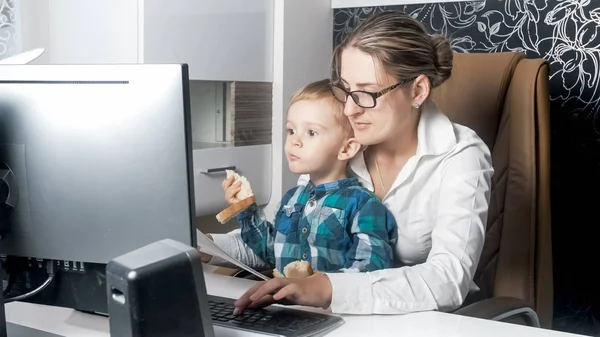 Jovem empresária trabalhando em casa enquanto seu filho bebê comendo pão — Fotografia de Stock