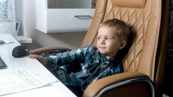 Portret chłopca śliczny maluch siedząc w wielkim skórzanym fotelu szefa w biurze — Zdjęcie stockowe