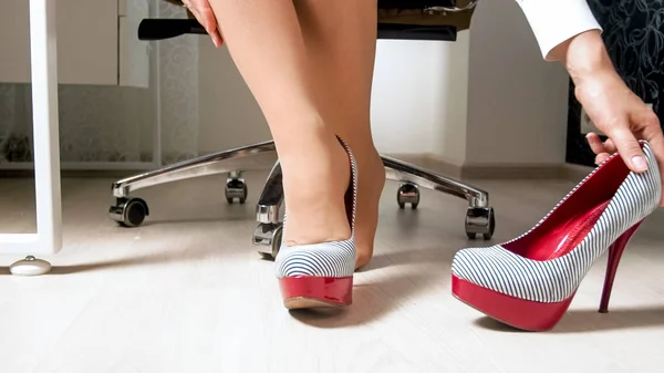 Hermosa mujer joven en pantimedias quitándose zapatos de tacón alto sexy debajo del escritorio en la oficina — Foto de Stock