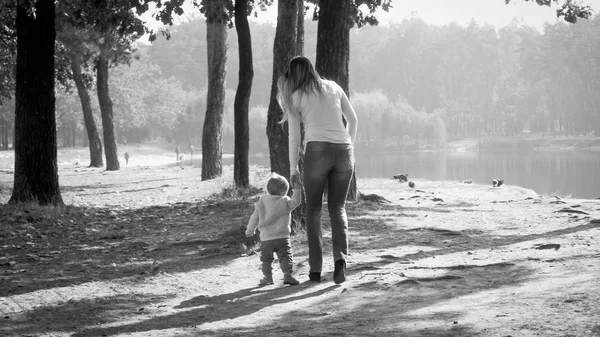 Schwarz-Weiß-Foto einer jungen Mutter, die ihren kleinen Sohn im Herbstpark spazieren führt — Stockfoto