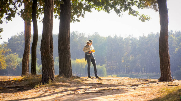Young woman with her toddler son standing in forest and looking at lake