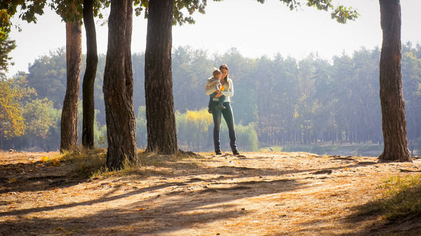 Happy smiling young woman embracing her toddler son at autumn park